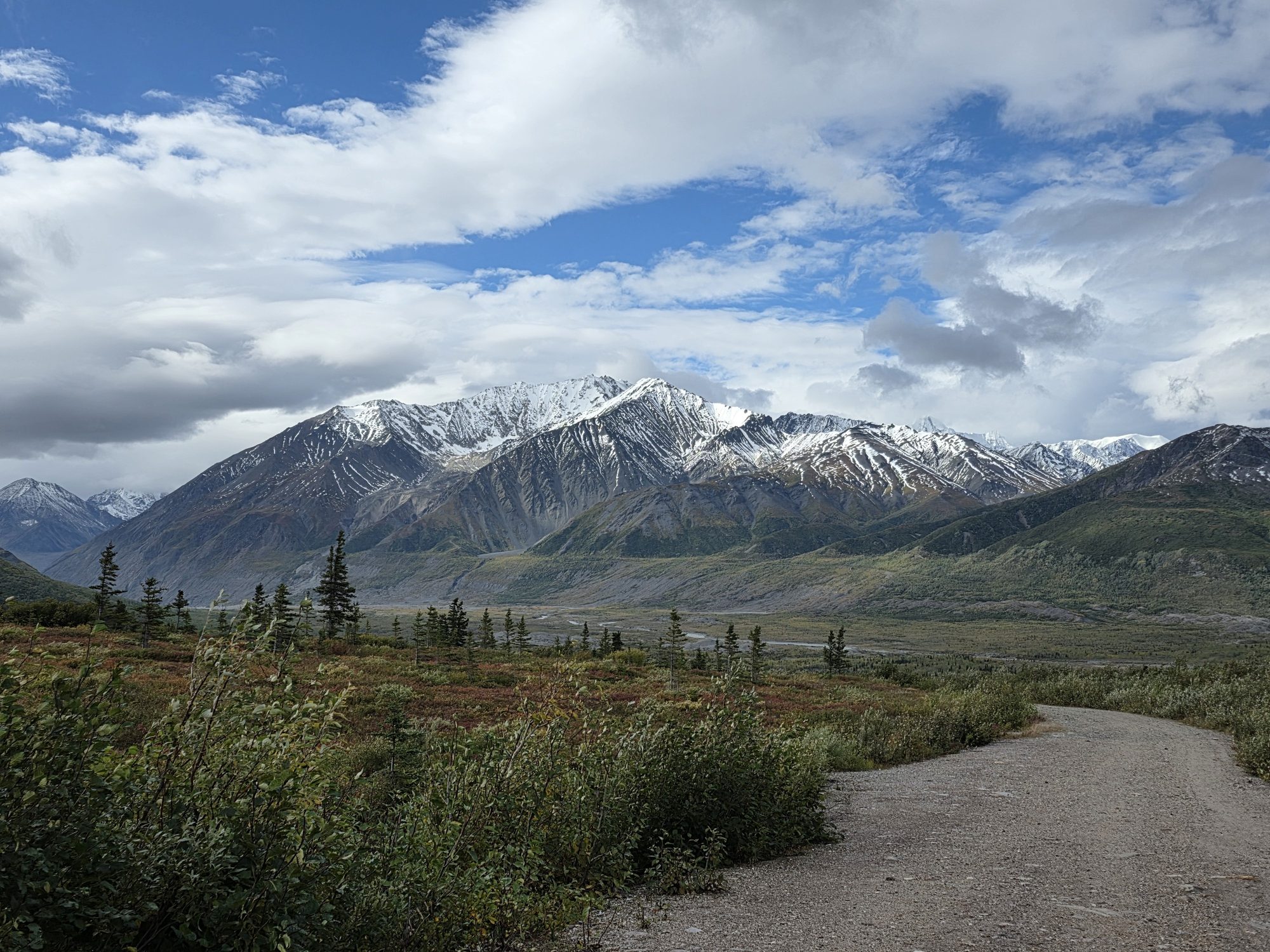 A gravel road leading toward snow-capped Alaska mountains