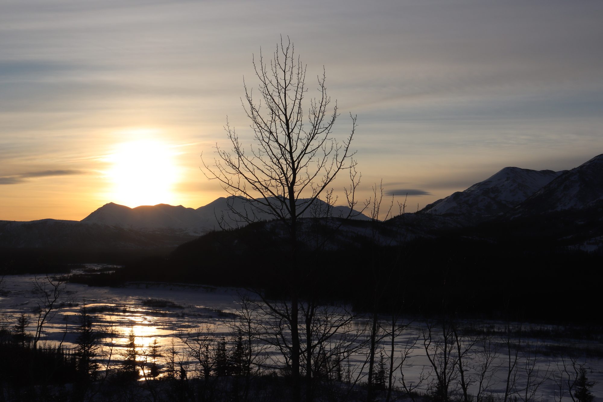 The sun setting over Alaska mountains and a river